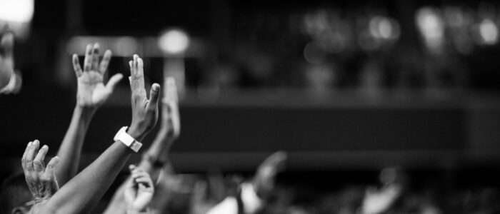 Black and white image of audience with hands raised, capturing concert energy.